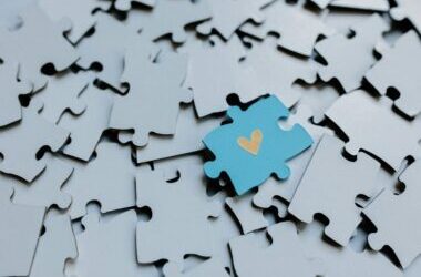 A single blue puzzle piece with a heart amid scattered pieces, symbolizing connection.